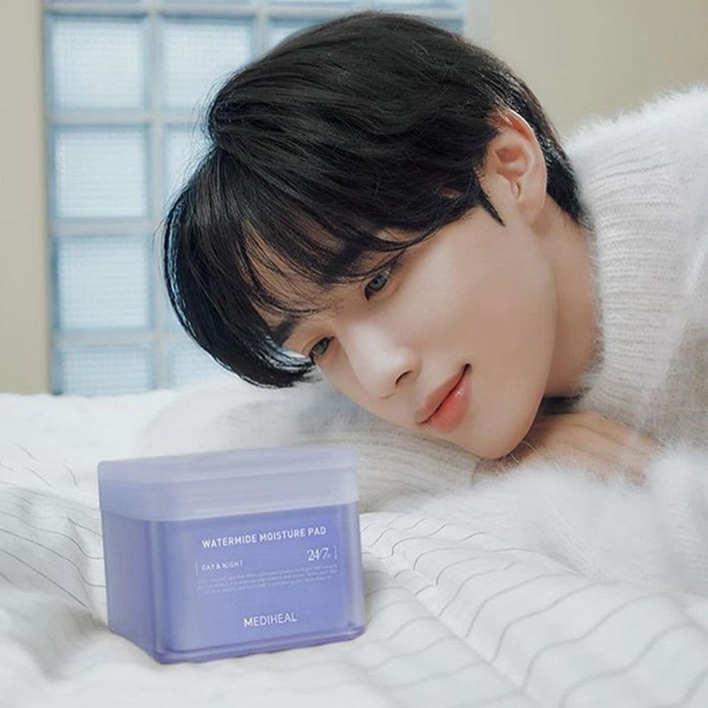 Un uomo è sdraiato accanto a una scatola quadrata. Scritta: Watermide Moisture Pad, Day & Night, 24/7, Mediheal. Scatola viola.