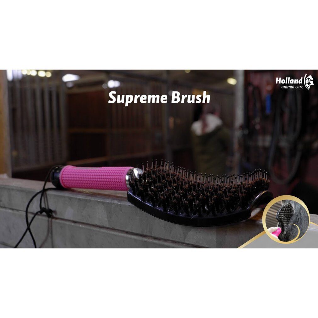 Spazzola con manico rosa e testina nera. Nome del prodotto: Supreme Brush. Sullo sfondo si vede una stalla.