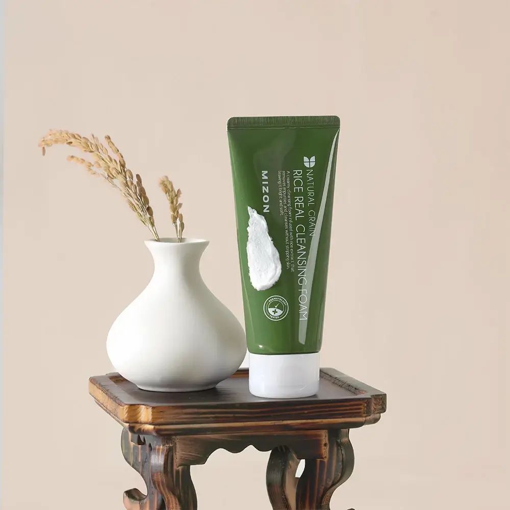 Tubo verde con schiuma bianca accanto a vaso con spighe. Scritta: MIZON, NATURAL GRAIN RICE REAL CLEANSING FOAM.