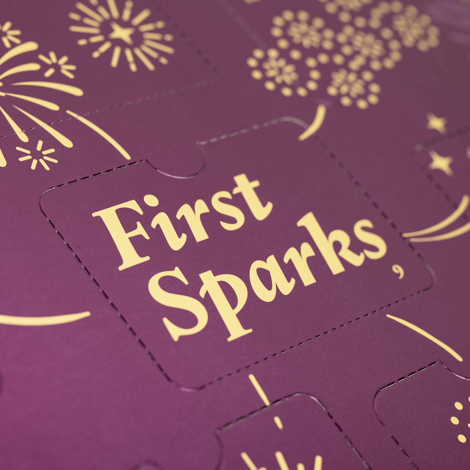 Primo piano del calendario dell'Avvento. Testo dorato: First Sparks. Illustrazioni di fuochi d'artificio.