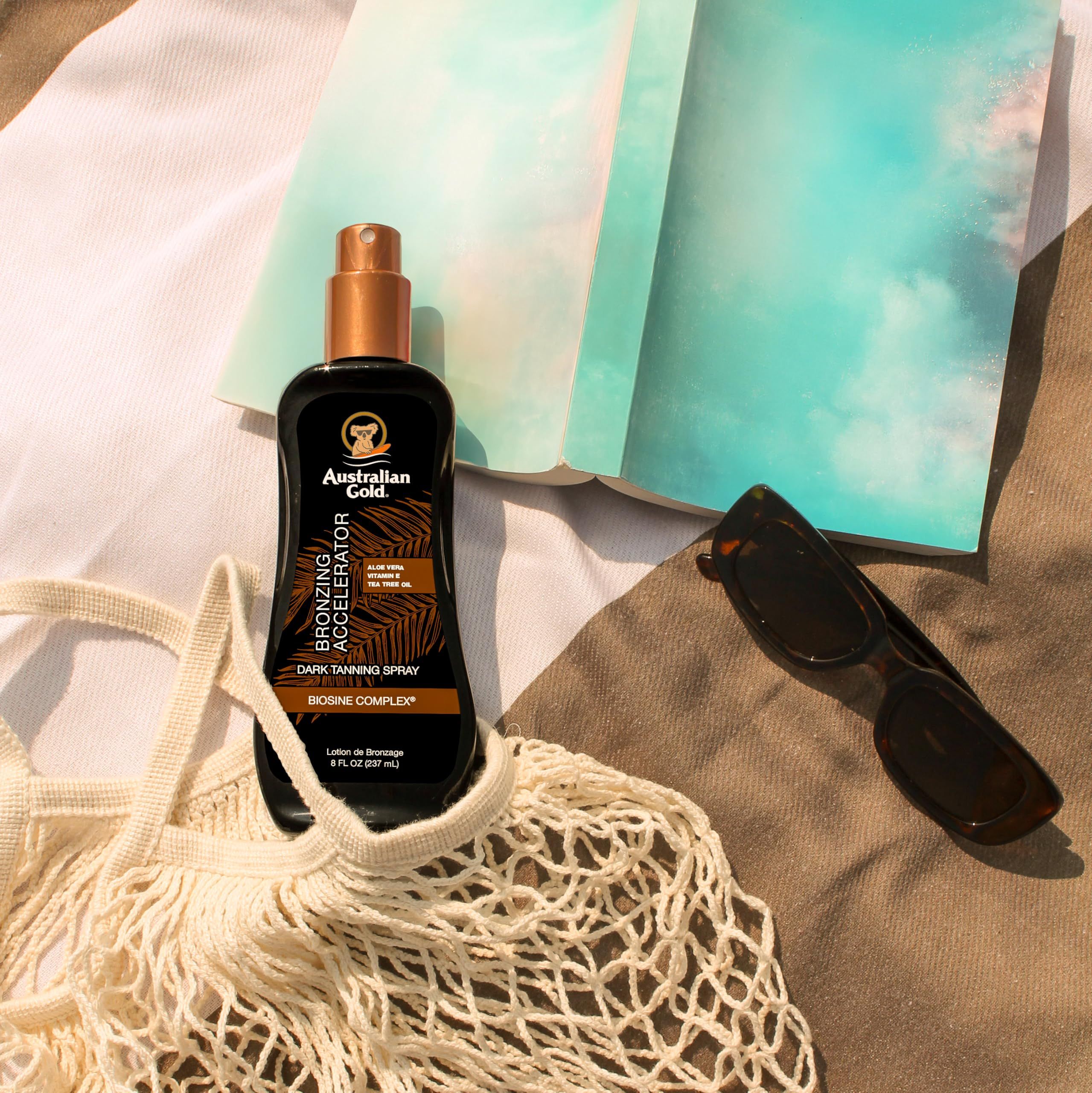 Gel spray abbronzante su un telo da spiaggia. Accanto, occhiali da sole e taccuino. Scritta: Australian Gold, Bronzing Accelerator.