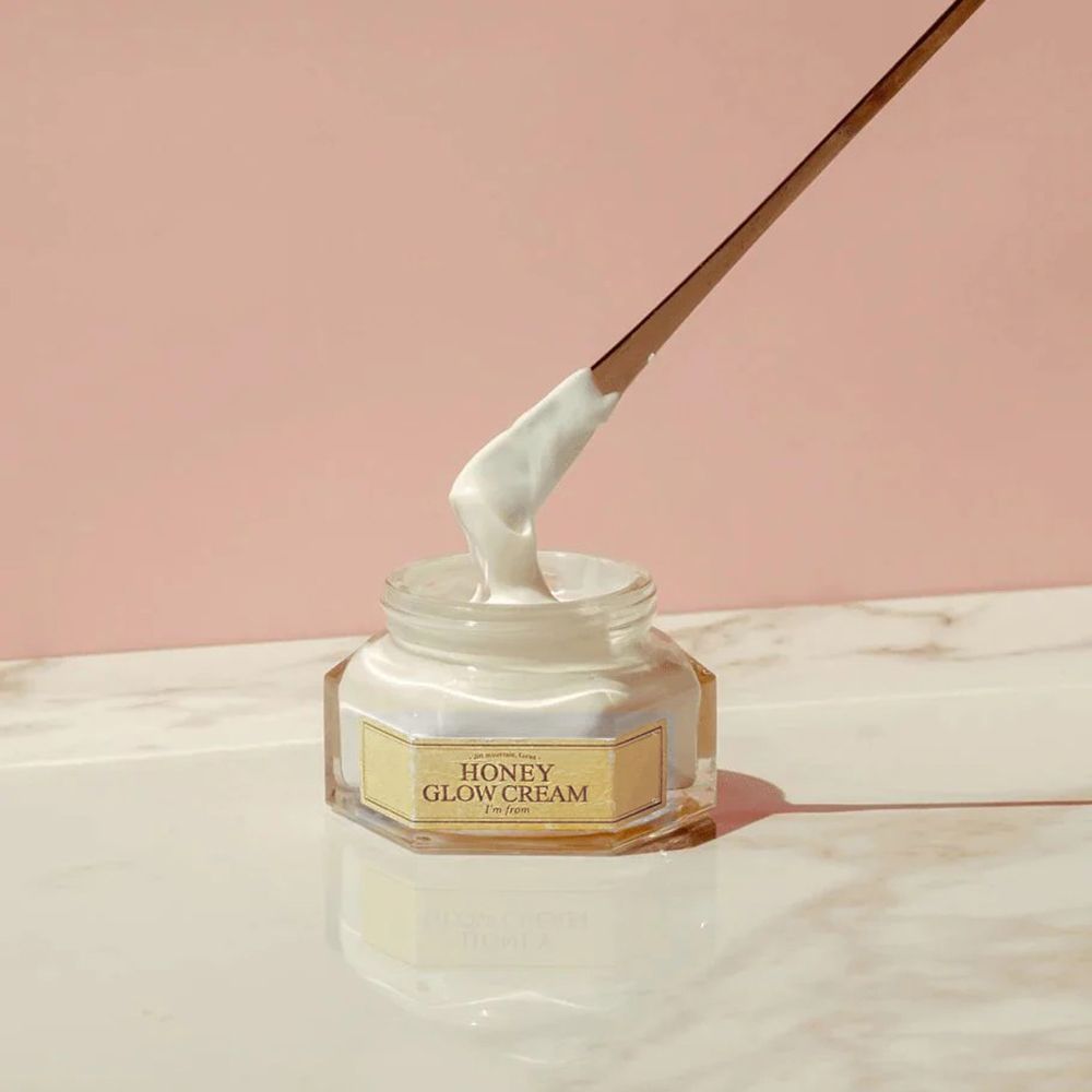Vasetto di crema e spatola. Scritta: HONEY GLOW CREAM, I'm from. Crema prelevata con spatola. Sfondo rosa.