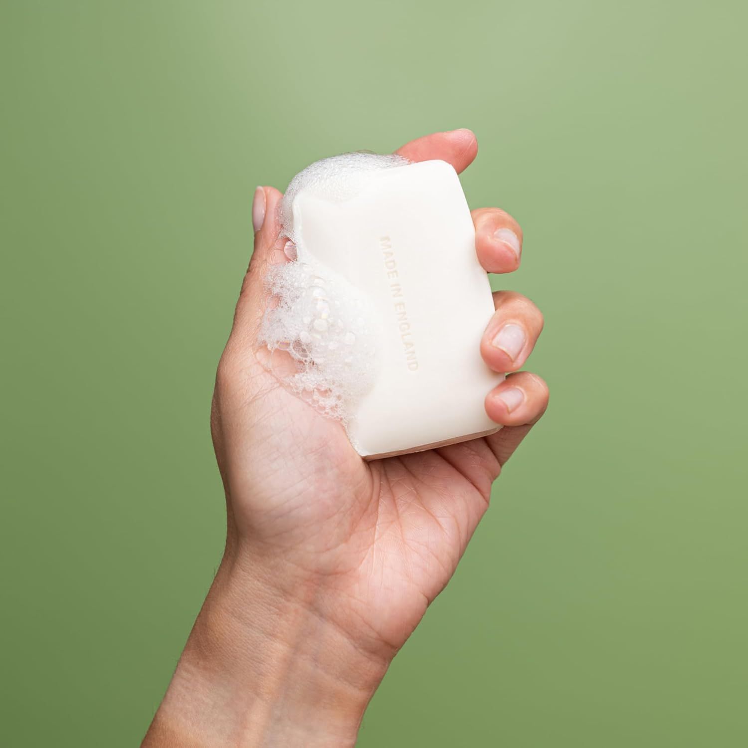 Una mano tiene una saponetta con schiuma. Il sapone è rettangolare e bianco.