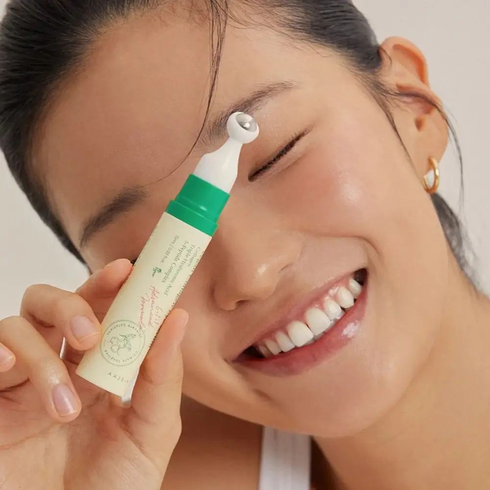 Donna che tiene in mano un siero occhi con applicatore roll-on. Sorride. AXIS-Y Vegan Collagen Eye Serum.