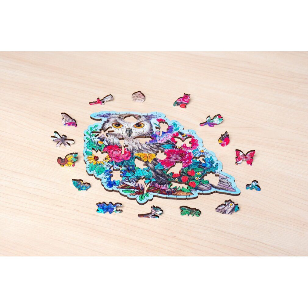 Puzzle con gufo e fiori, parzialmente assemblato. Singoli pezzi sparsi su superficie in legno.
