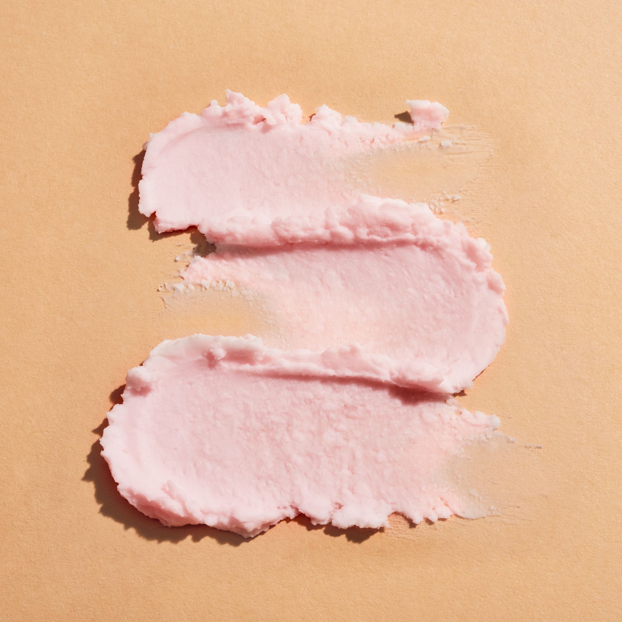 Due strisce di crema rosa su sfondo beige. Consistenza visibile.