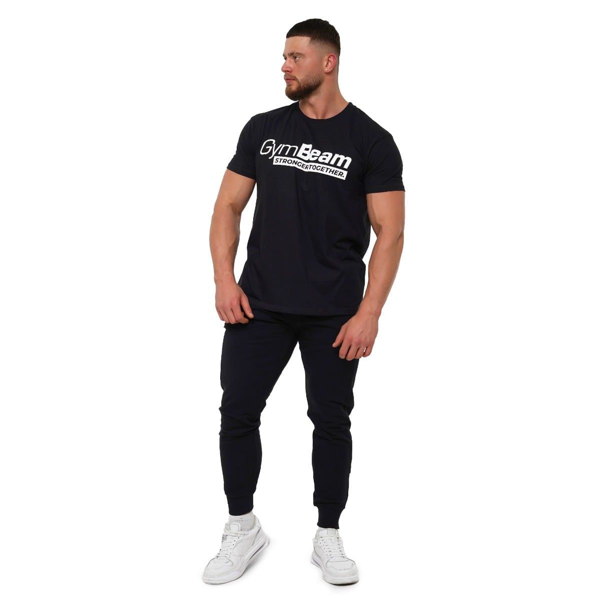 Uomo con t-shirt nera GymBeam e pantaloni della tuta, vista a figura intera.