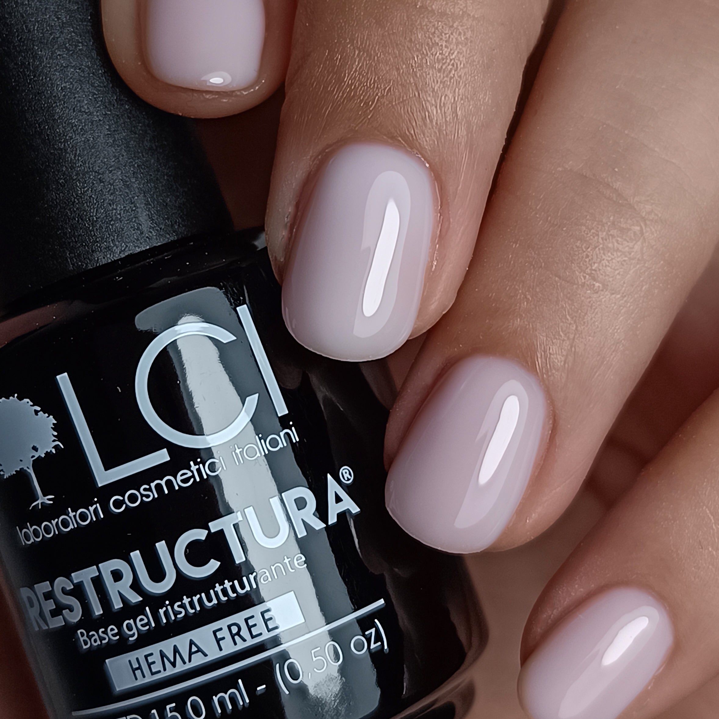 Primo piano di unghie smaltate. Scritte: LCI, Restructura, HEMA FREE. Lo smalto è rosa chiaro.