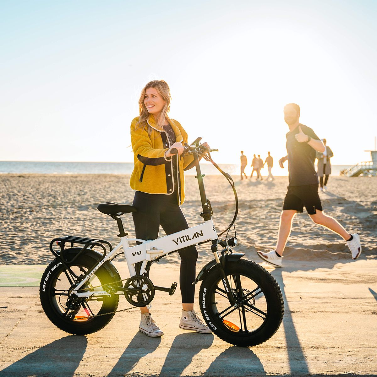 E-bike pieghevole bianca, pneumatici neri. Donna accanto. Vitilan V3 sul telaio.