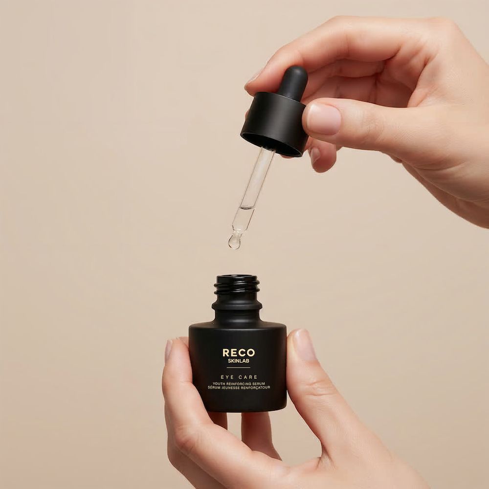 Mani che tengono un flacone nero RECO SKINLAB. Contagocce inserito nel flacone. Scritta: Eye Care Serum.