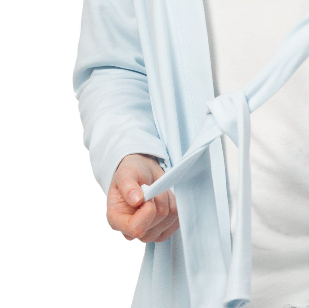 Primo piano: Accappatoio in cotone azzurro con cintura. Persona che annoda la cintura.