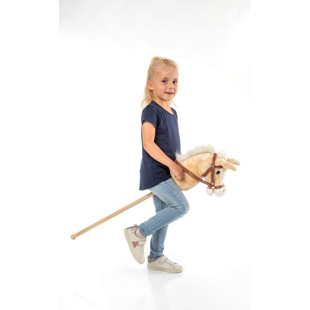 Bambina con cavallo a dondolo. Cavallo in peluche color crema, finimenti marroni. Manico in legno. Indossa jeans e maglietta blu.