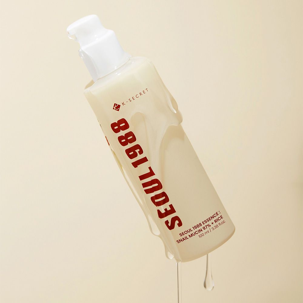 Flacone K-SECRET Seoul 1988 Essence inclinato, siero trasparente che cola. Flacone beige con scritta rossa.