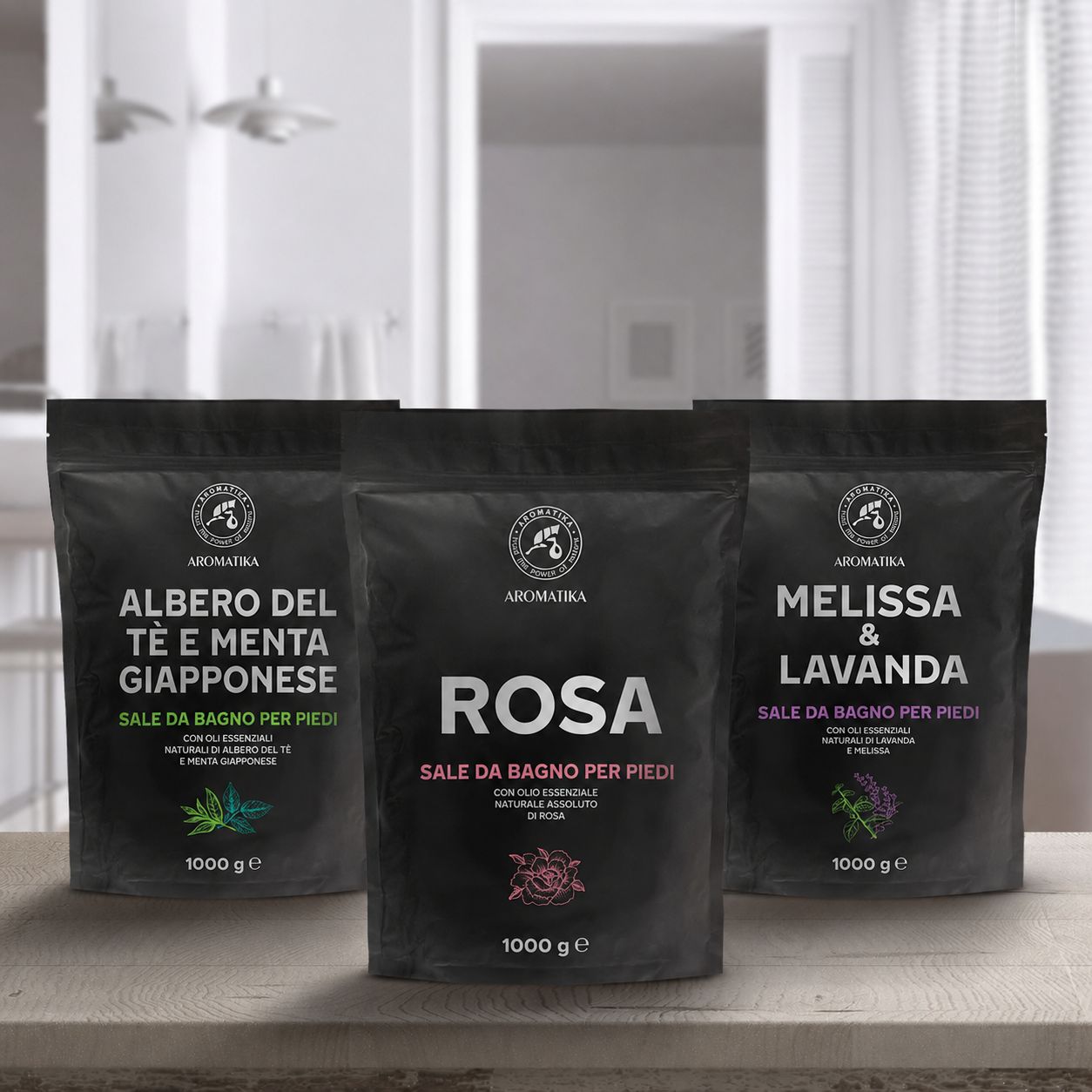 Tre sacchetti neri di sali da bagno per i piedi. Scritte: Tea Tree & Menta giapponese, Rosa, Melissa & Lavanda. Logo: Aromatica. 1000 g.