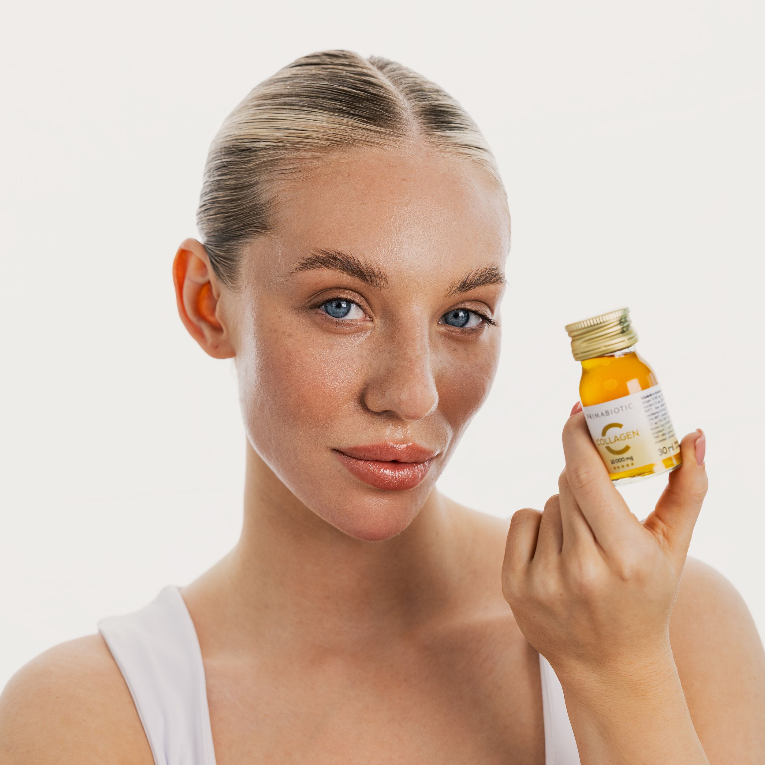 Donna che tiene in mano una bottiglia di Primabiotic Collagen. Tappo dorato, etichetta con scritta. Donna bionda con occhi blu.