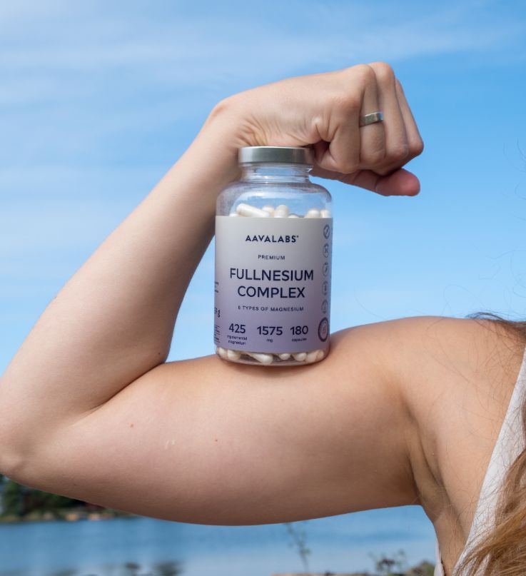 Donna che presenta la bottiglia Aavalabs Magnesium Komplex sul bicipite.