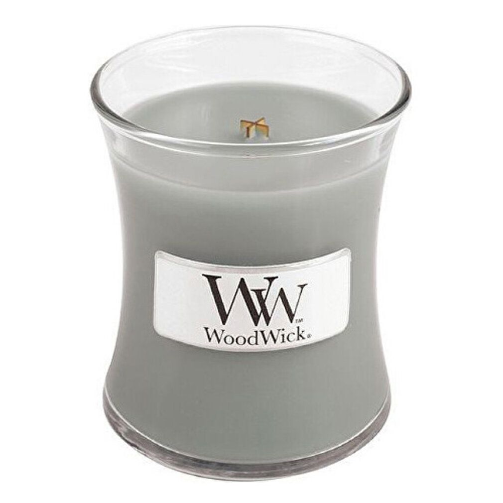 Candela a forma di clessidra. Cera grigia, etichetta WoodWick. Contenitore di vetro. Stoppino in legno visibile.