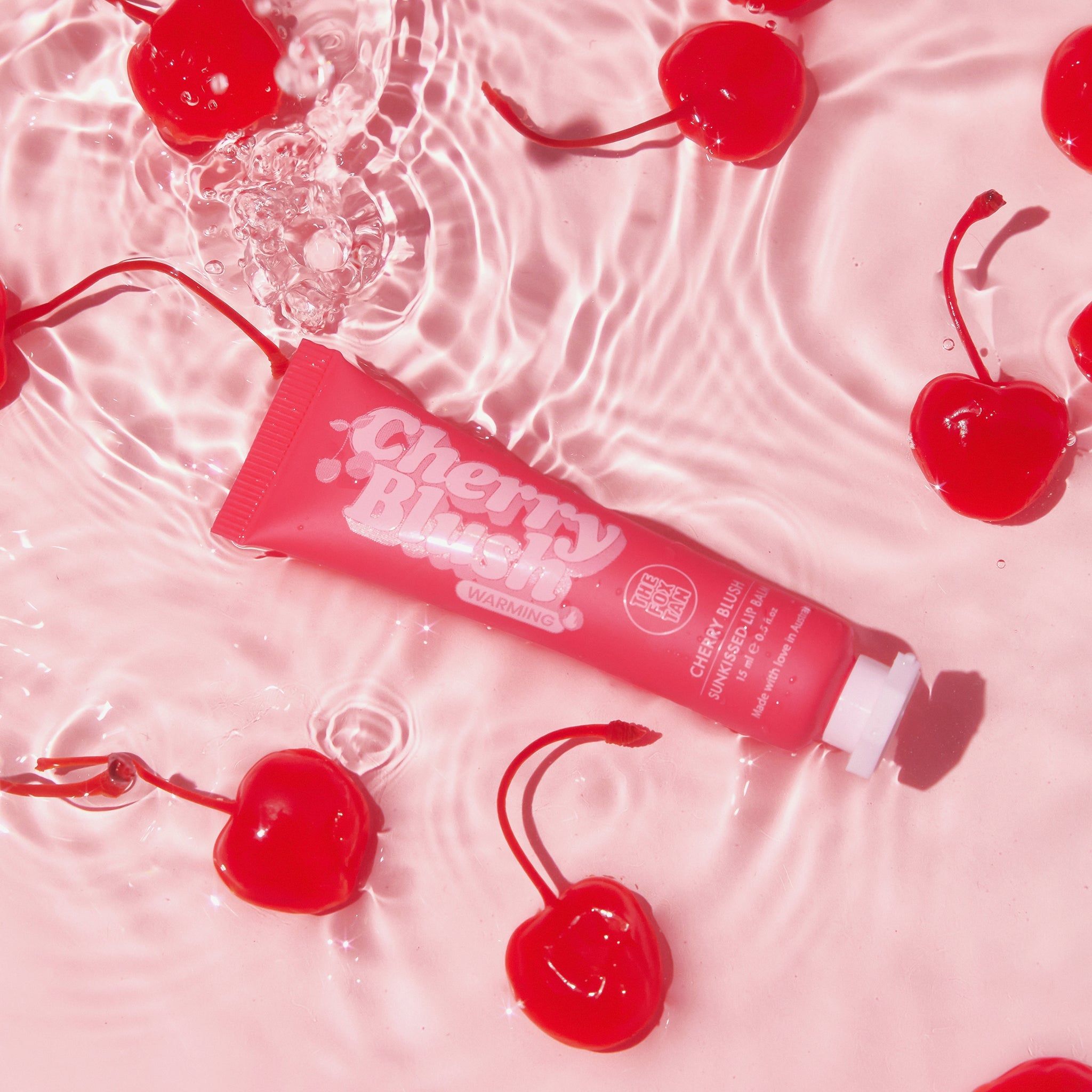 Tubo rosso 'Cherry Blush' in acqua con ciliegie. Nome del prodotto e marchio visibili. Tappo bianco.