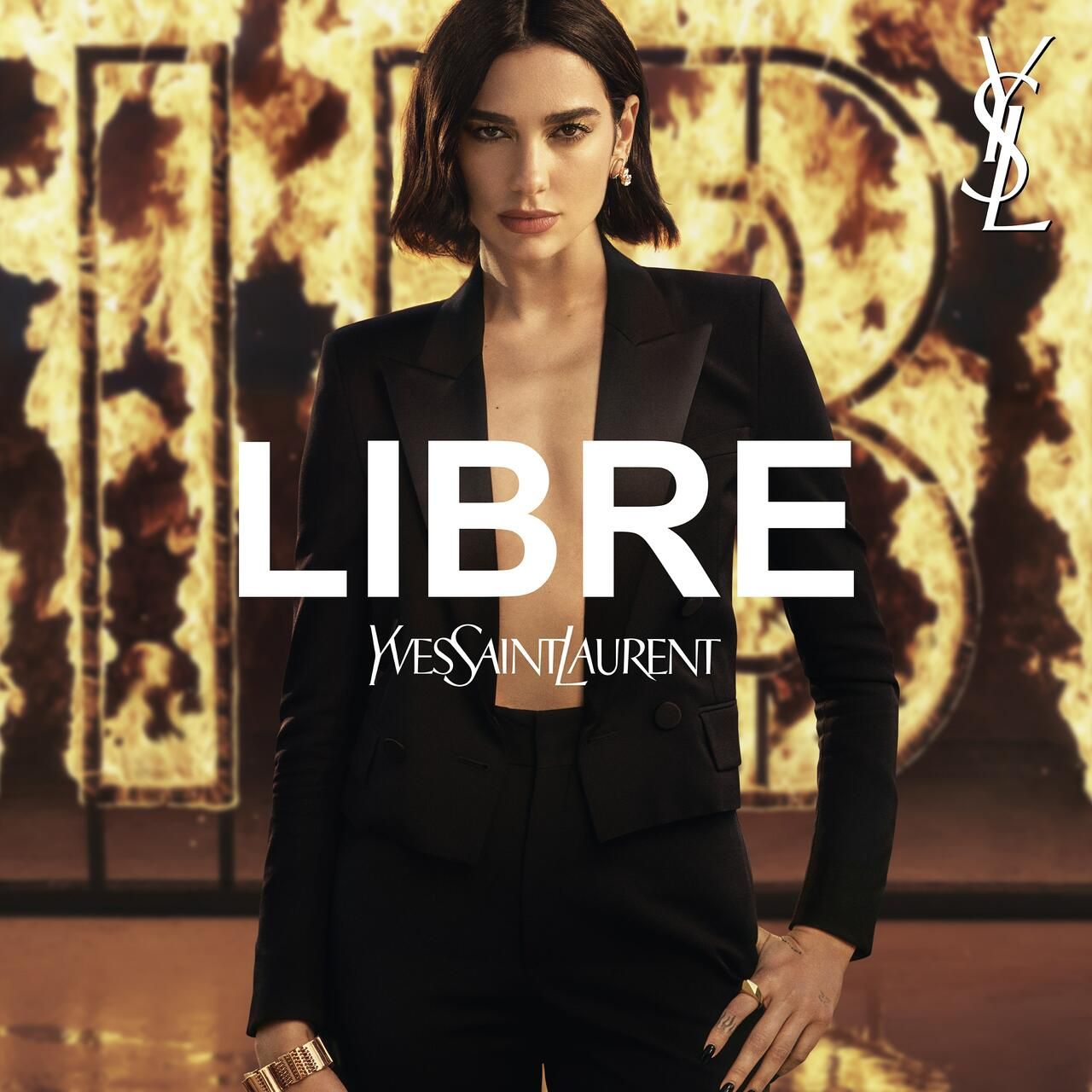 Donna in completo nero davanti a uno sfondo infuocato. Grande logo 'LIBRE' e logo Yves Saint Laurent.
