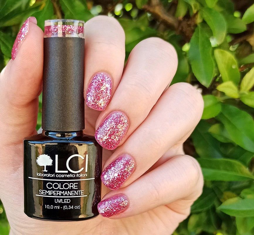 Flacone di smalto in mano. Unghie rosa glitterate. Scritte: LCI, Colore Semipermanente, UVLED.