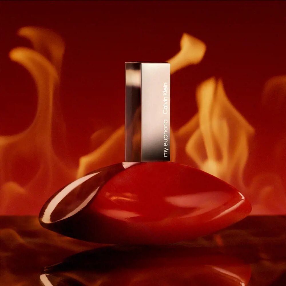 Flacone rosso con tappo argentato. Flacone a forma di goccia. Sfondo con fiamme. Scritta "my euphoria" e "Calvin Klein".