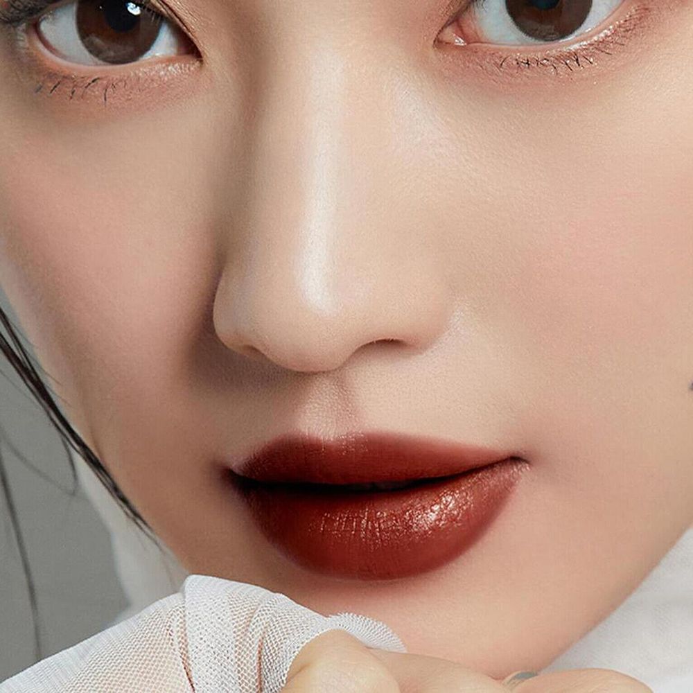 Lucidalabbra marrone scuro applicato sulle labbra. Primo piano di un viso. Carnagione chiara. Abbigliamento bianco.