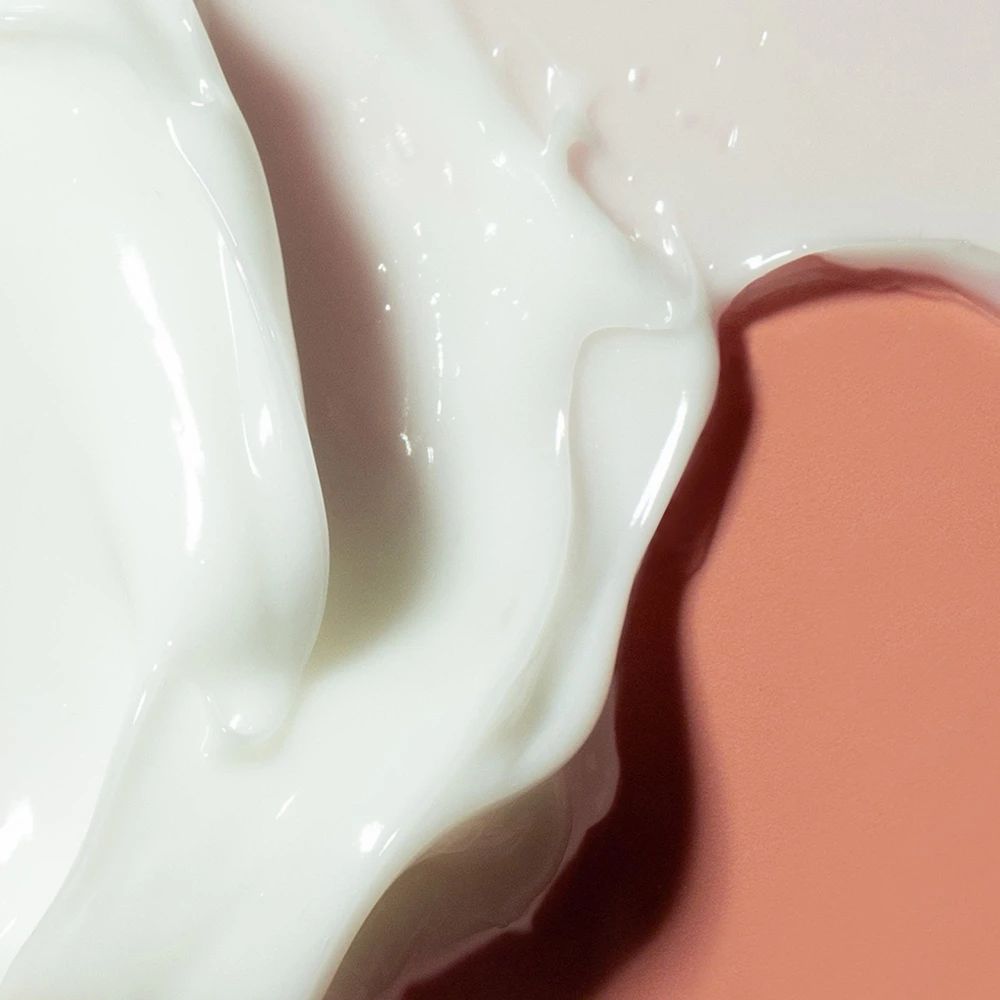 Primo piano di crema bianca su sfondo rosa. La crema ha una consistenza liscia e lucida.