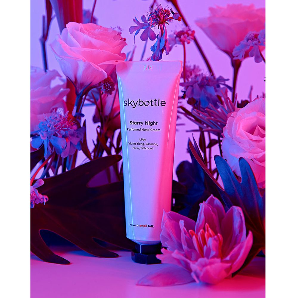 Tubo bianco di crema mani SKYBOTTLE Starry Night, circondato da fiori. Testo: Starry Night, Lilac, Ylang Ylang, Jasmine, Musk, Patchouli.