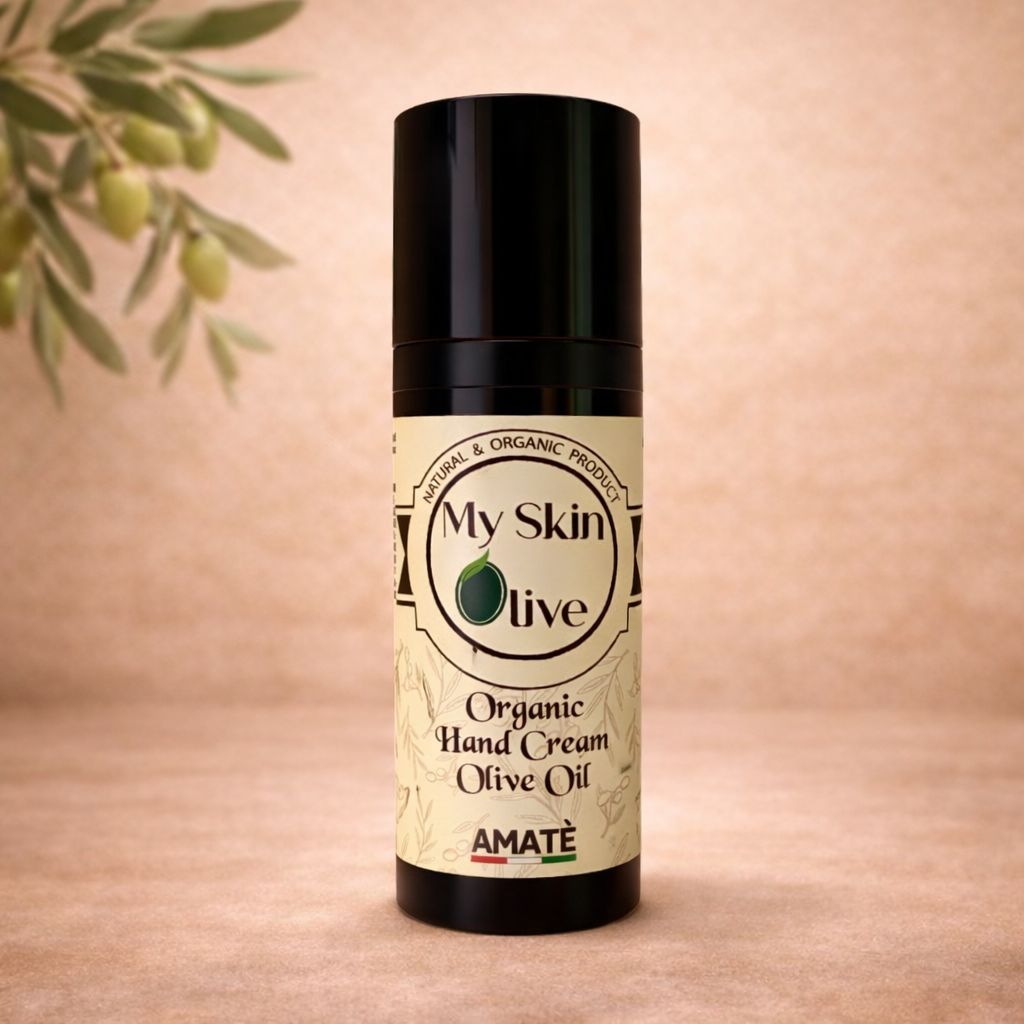 Flacone nero con etichetta. Scritta: My Skin Olive, Organic Hand Cream Olive Oil, Amatè. Sfondo con ramo d'ulivo.