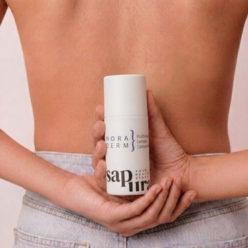 Flacone dispenser bianco con loghi 'Nora Derm' e 'SAPURA', tenuto dietro la schiena di una persona.
