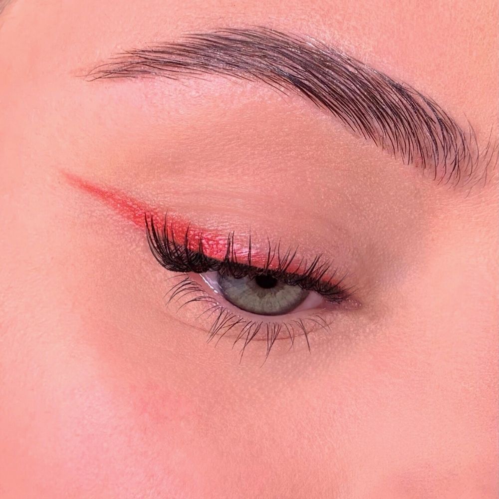 Occhio con eyeliner rosso. Palpebra superiore con eyeliner rosso. Ciglia e sopracciglia visibili.