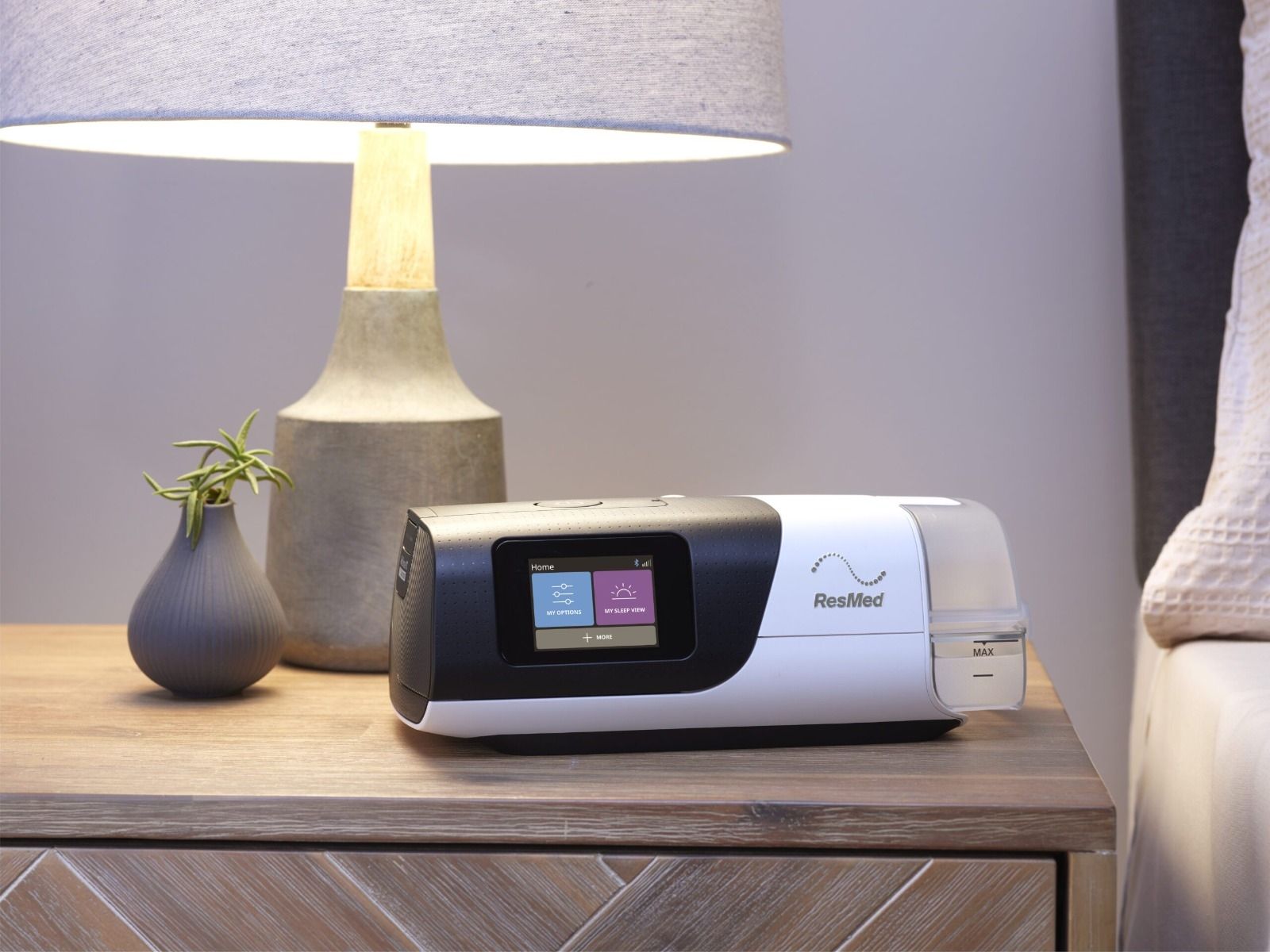 ResMed AirSense 11 su un comodino accanto a una lampada e un vaso.