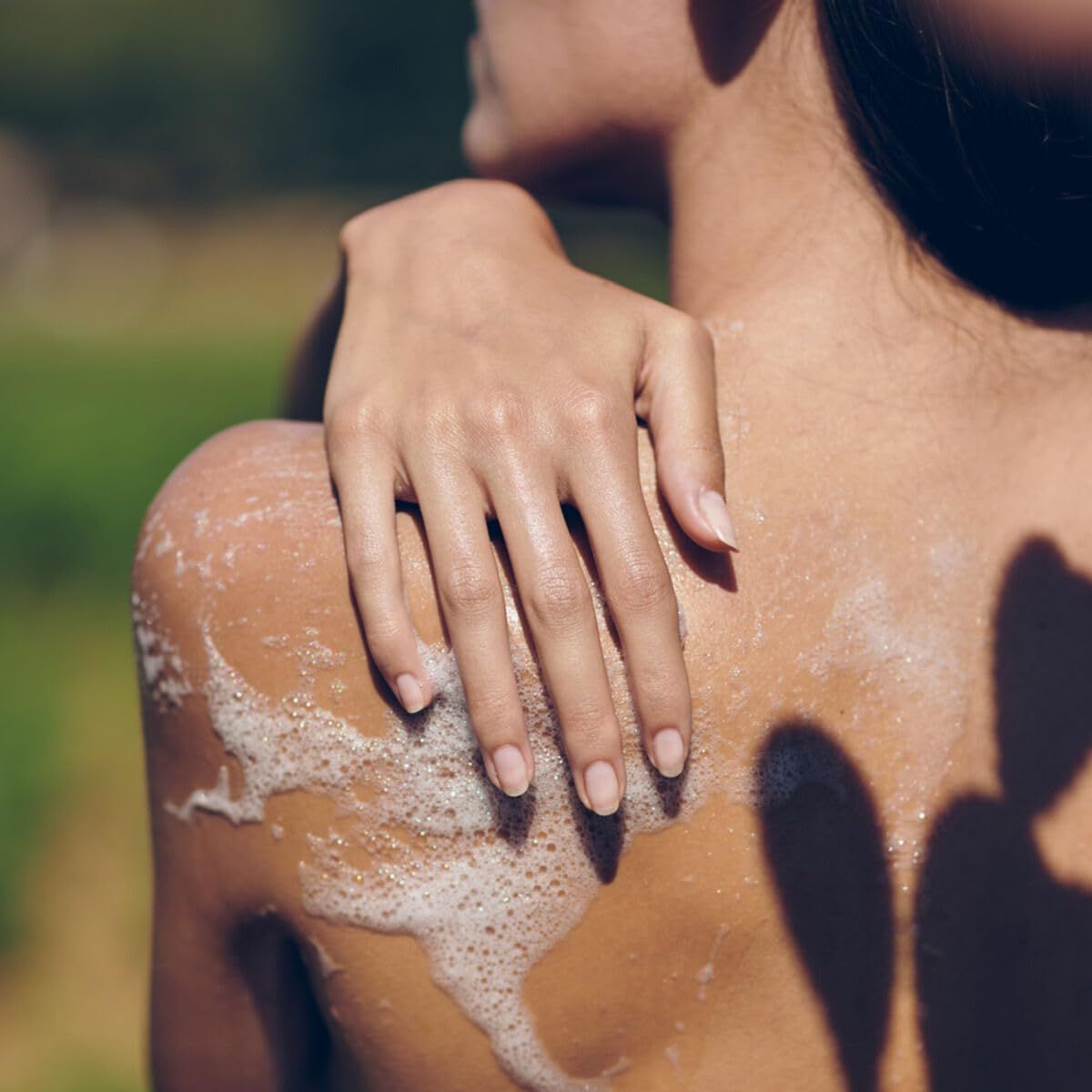 Schiena di una persona con schiuma saponosa. Una mano è appoggiata sulla spalla.