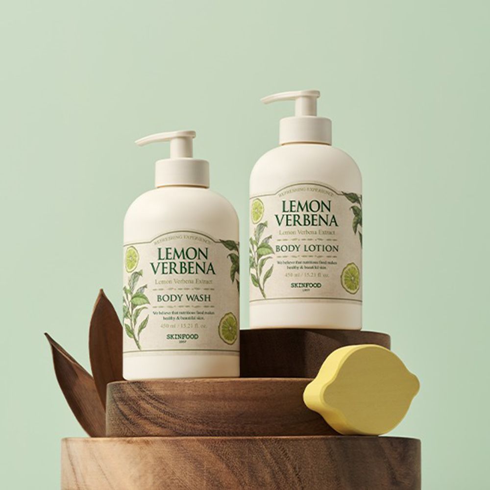 Due flaconi con dosatore. Scritta: Lemon Verbena Body Wash e Body Lotion. Su piedistallo in legno, sfondo verde.