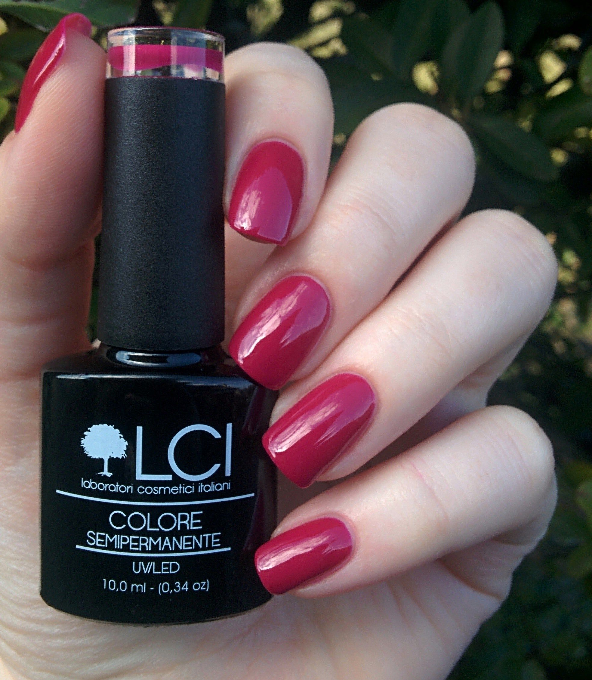Mano che tiene un flacone di smalto e unghie smaltate rosa scuro. Scritta: LCI, Colore Semipermanente, UVLED.