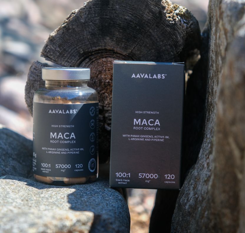 Flacone e scatola di capsule di Maca accanto a pietre e legno.
