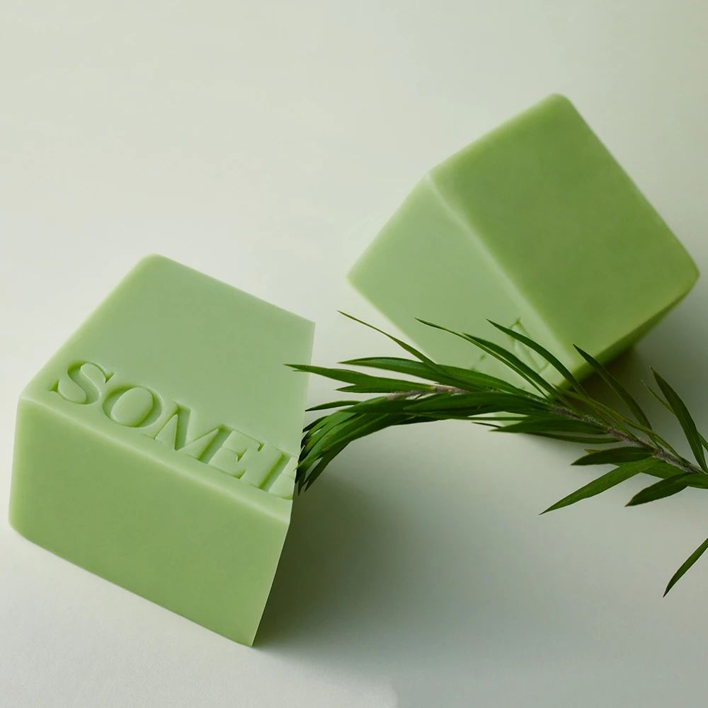 Due panetti di sapone verdi con scritta 'SOMEBYMI' e un rametto.