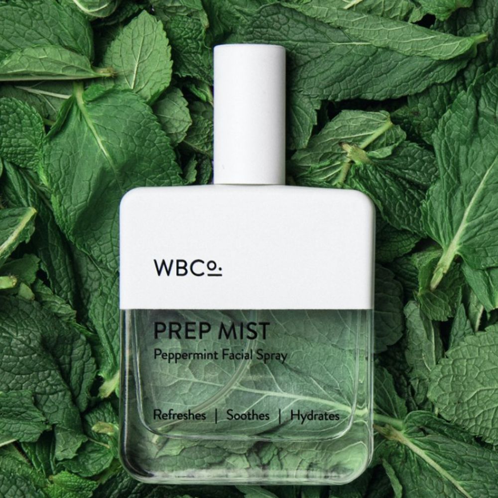 Flacone spray trasparente con tappo bianco. Scritta: WBCo., PREP MIST, Peppermint Facial Spray. Su foglie di menta.