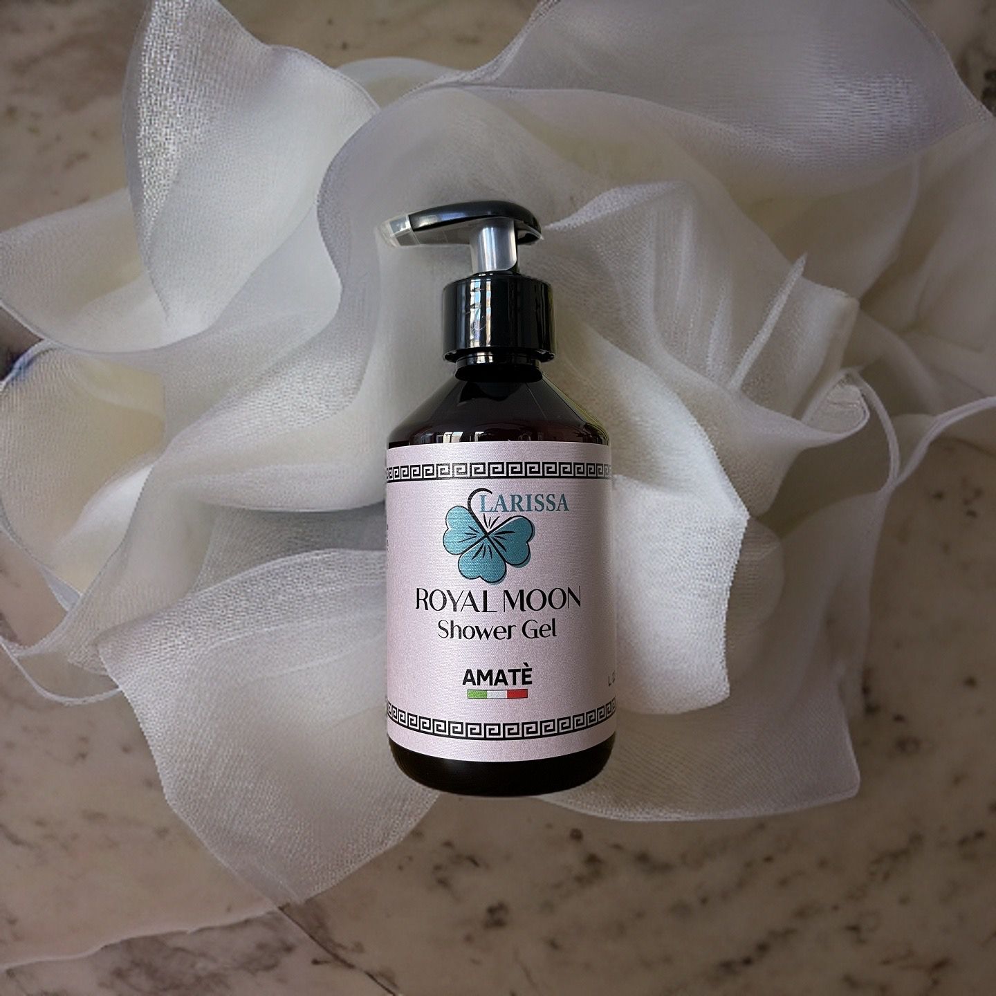 Flacone marrone con dosatore. Etichetta "Larissa Royal Moon Shower Gel" e "Amatè". Su tessuto bianco.
