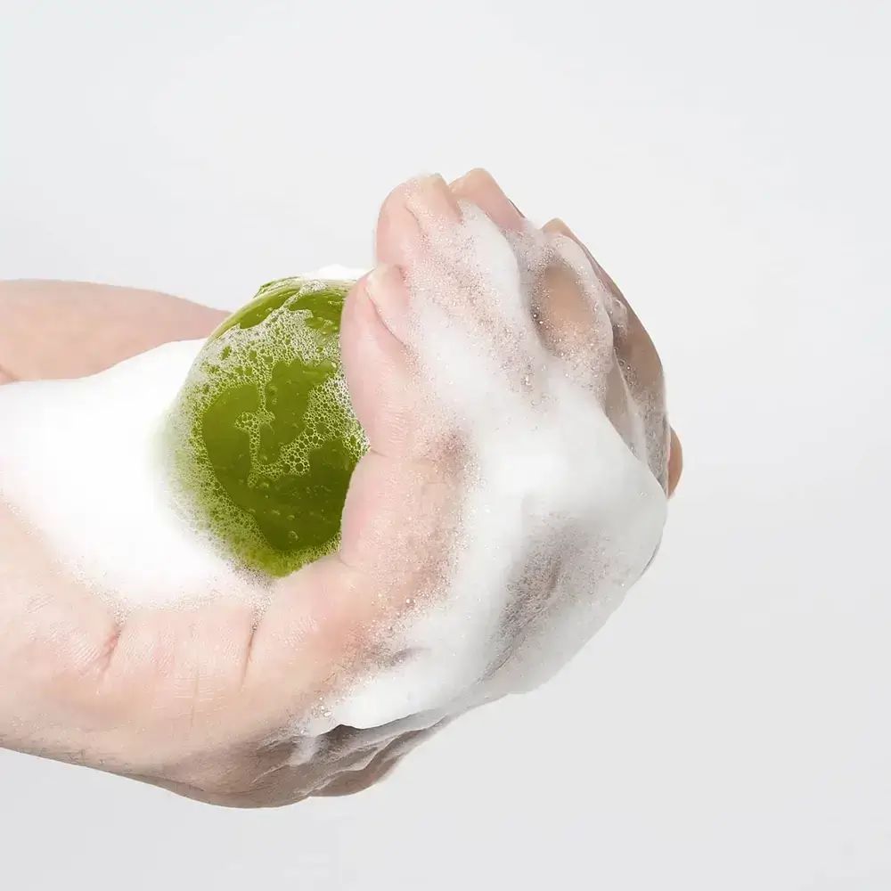 Oggetto sferico verde in mano, circondato da schiuma.