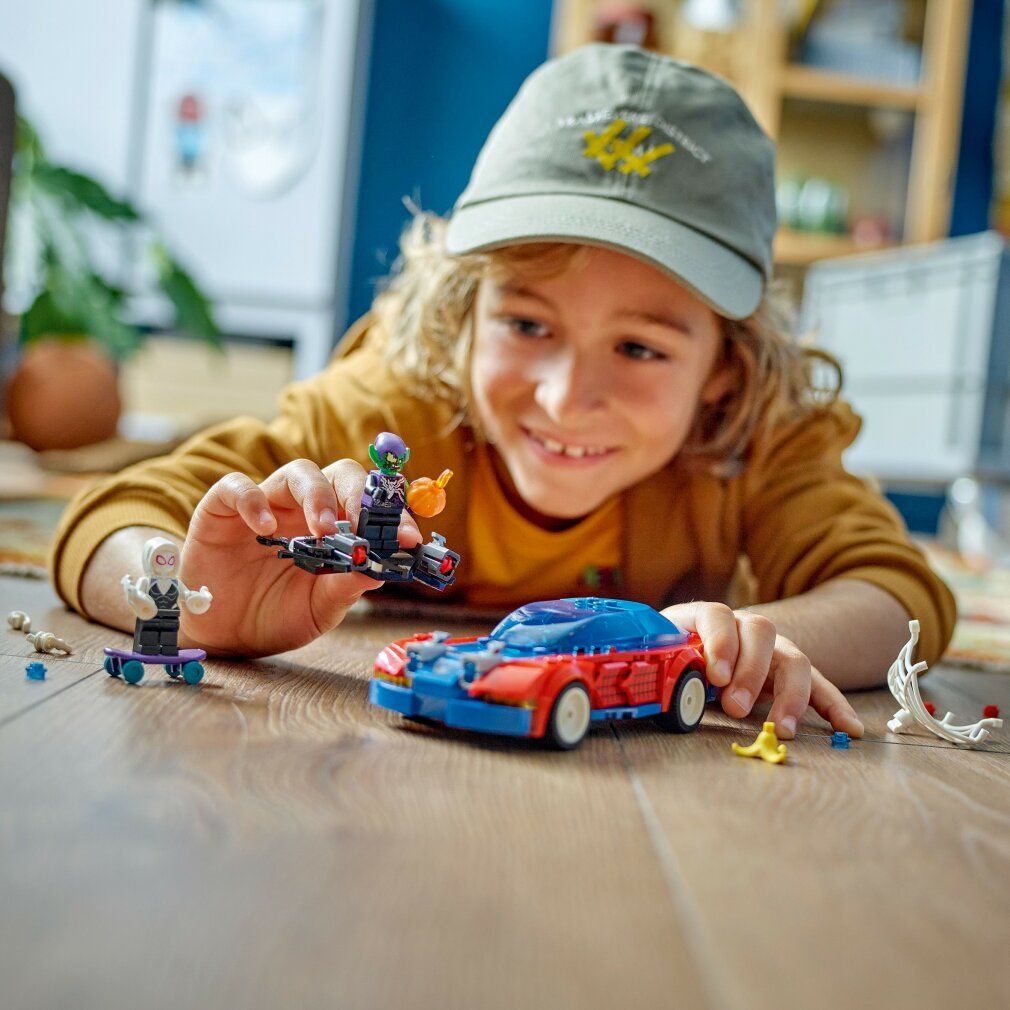 Bambino che gioca con il set LEGO Marvel. Auto rossa e blu, personaggi di Ghost Spider e Green Goblin, ragnatela.