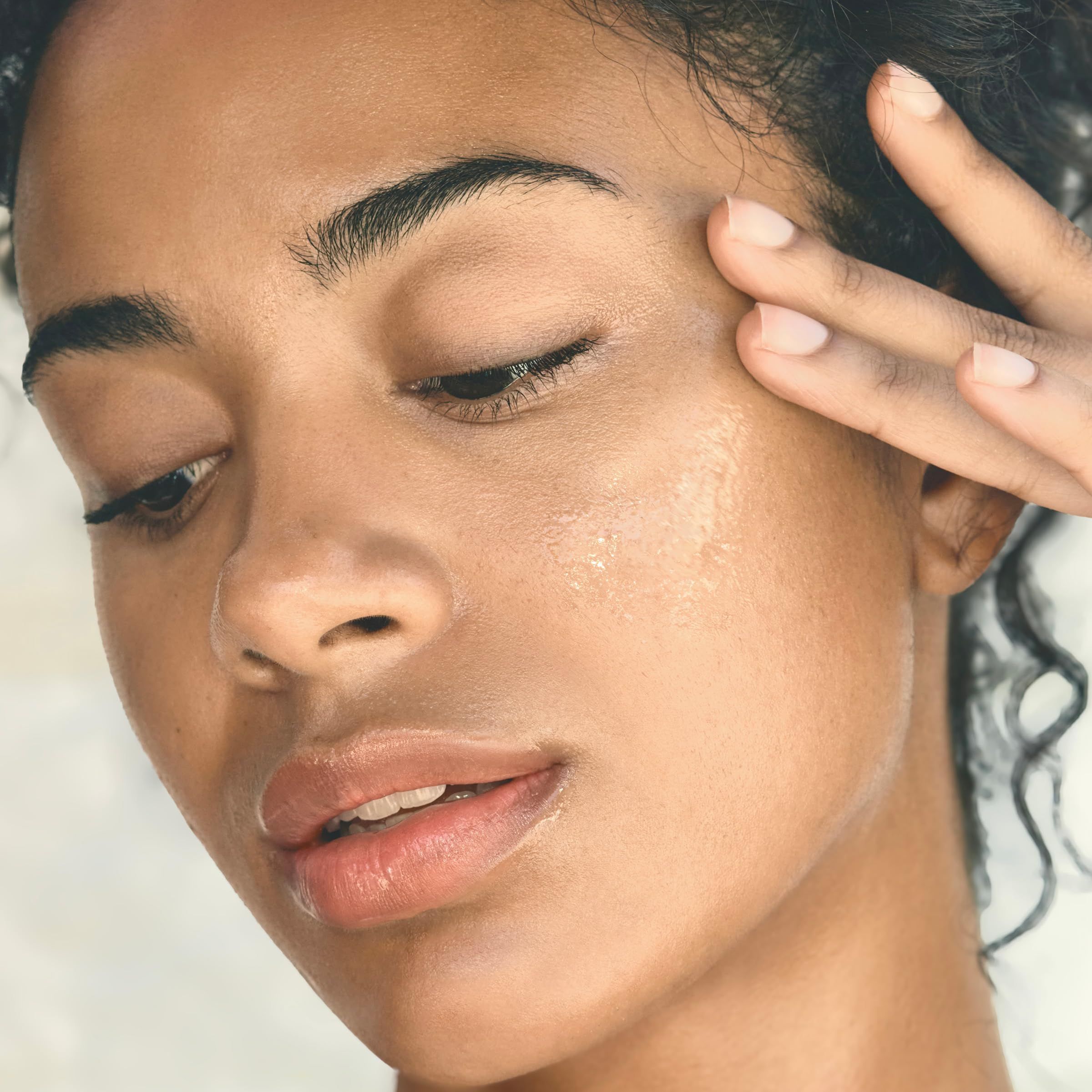 Primo piano di una donna che si tocca il viso. Pelle con idratazione visibile. Luce naturale.