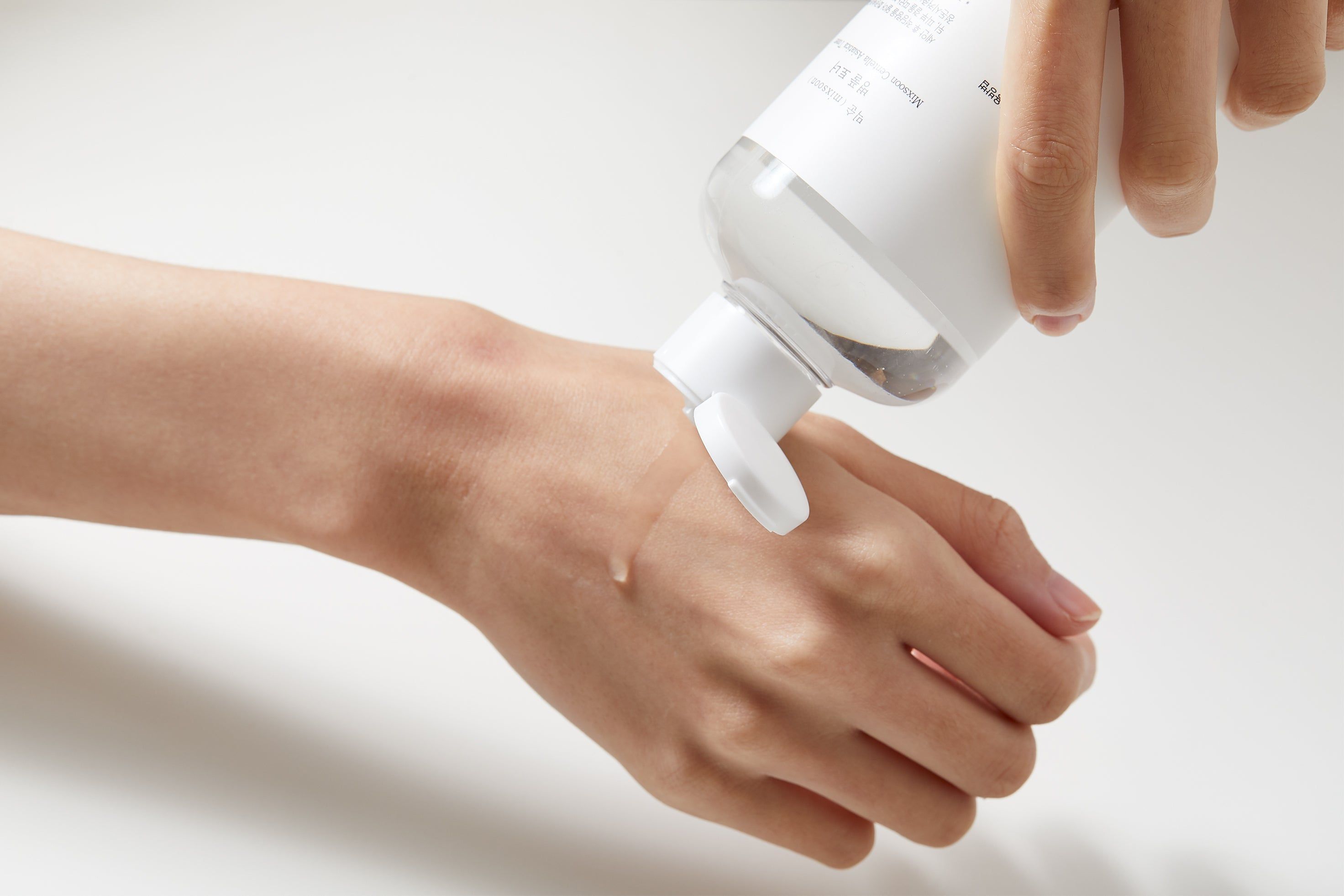 Una mano versa del liquido da un flacone sul palmo. Sul flacone si legge "mixsoon".