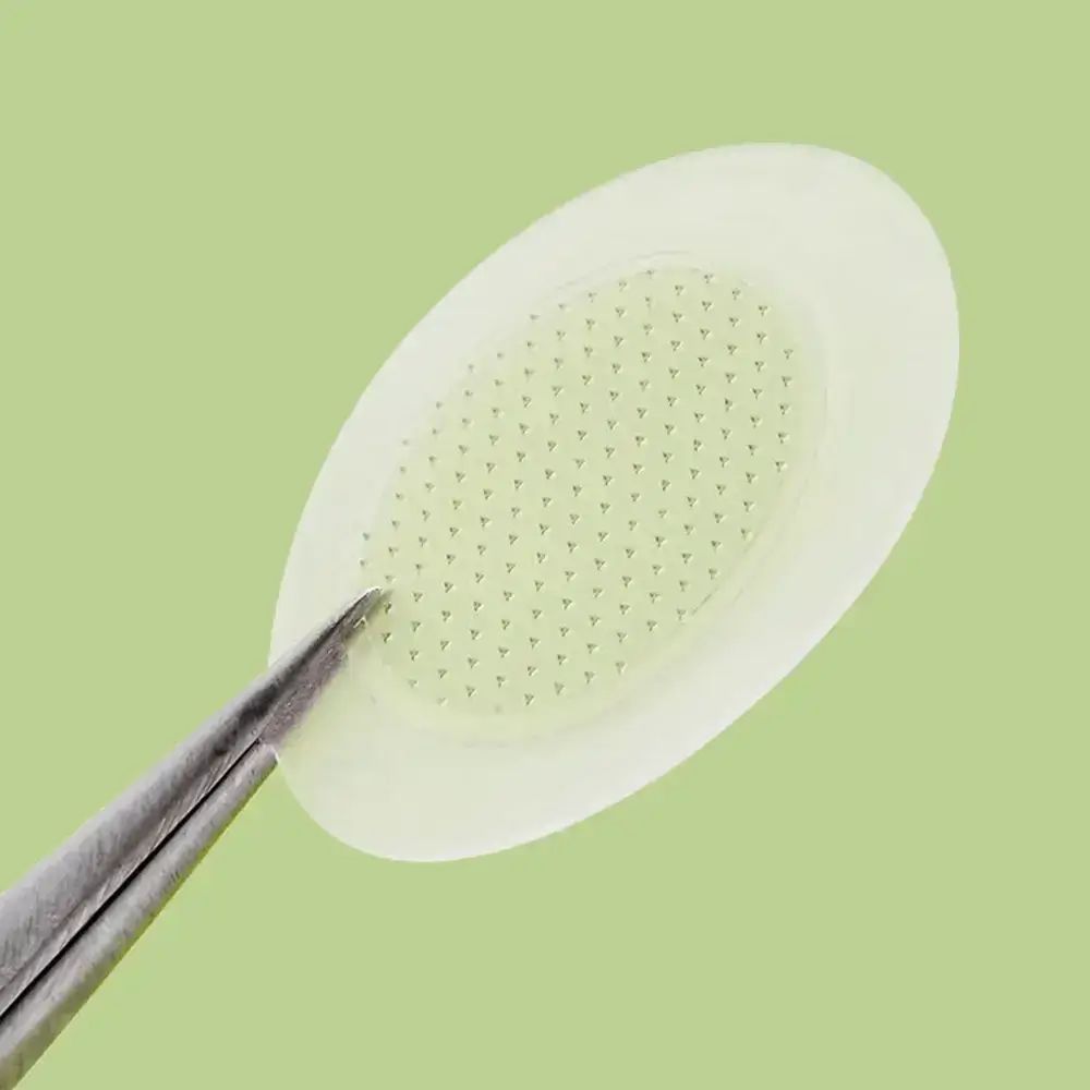 Primo piano di un cerotto con micro-punte. Pinzetta che afferra il cerotto. Sfondo verde.