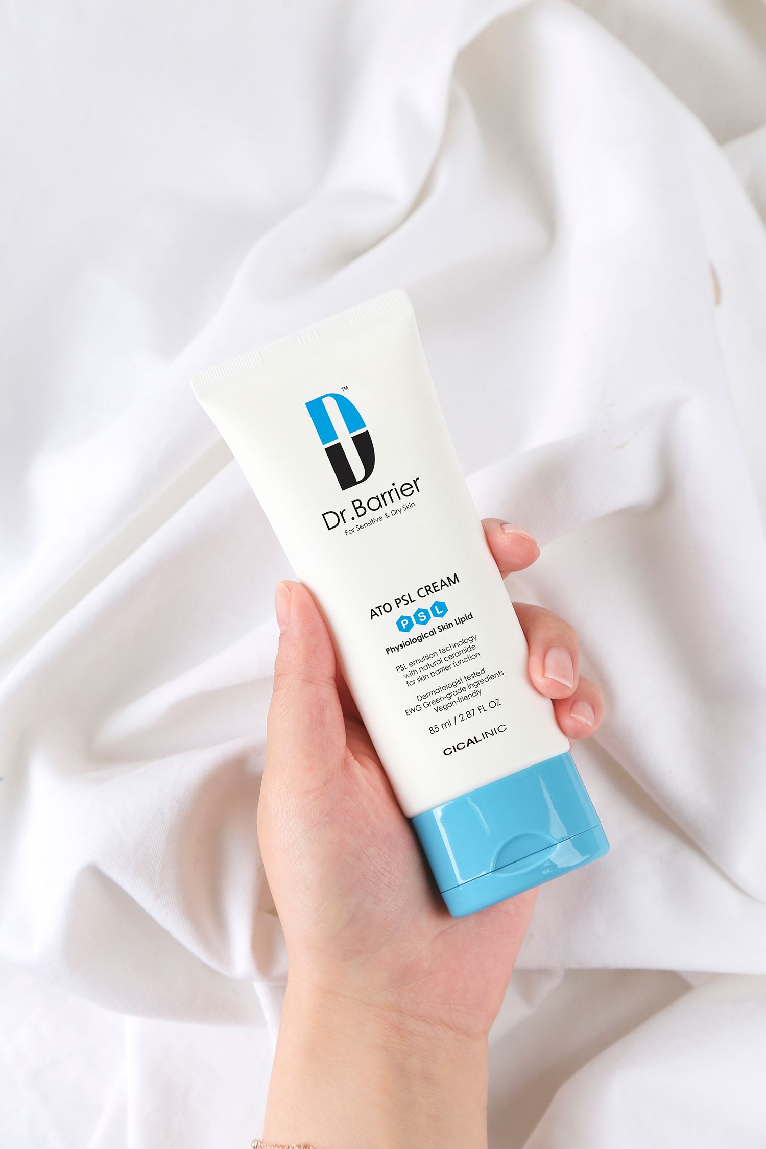 Un tubo di Dr.Barrier ATO PSL Cream. Tenuto in mano, su tessuto bianco. Tubo bianco con tappo blu.