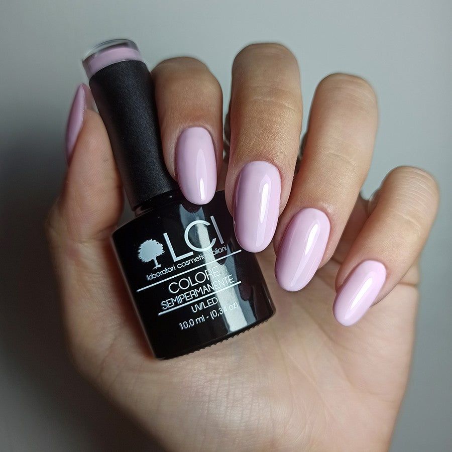 Mano con unghie smaltate e flacone di smalto. Smalto rosa. Scritta: LCI, Colore Semipermanente, UVLED 10,0 ml.