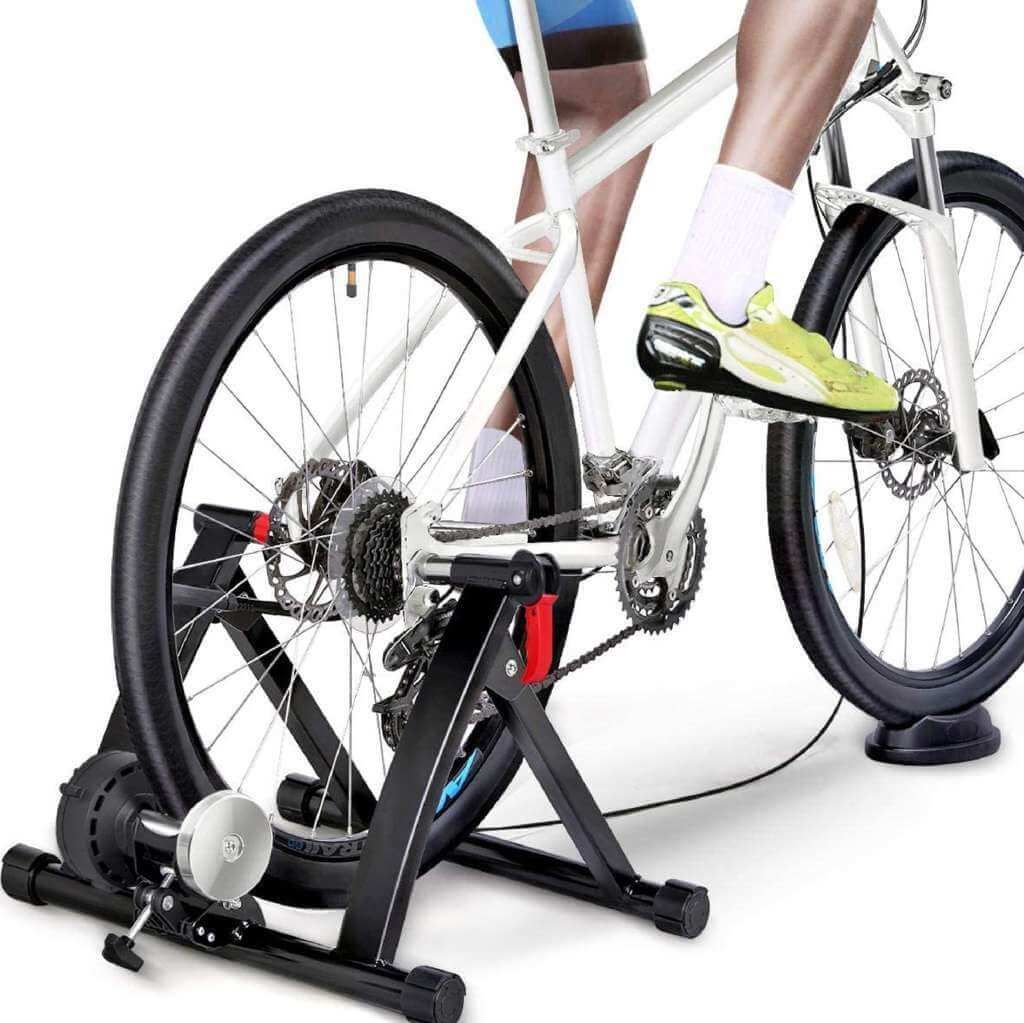 Bicicletta su un rullo per bici nero. Persona che va in bicicletta. Il rullo ha un rullo che tocca la ruota posteriore.