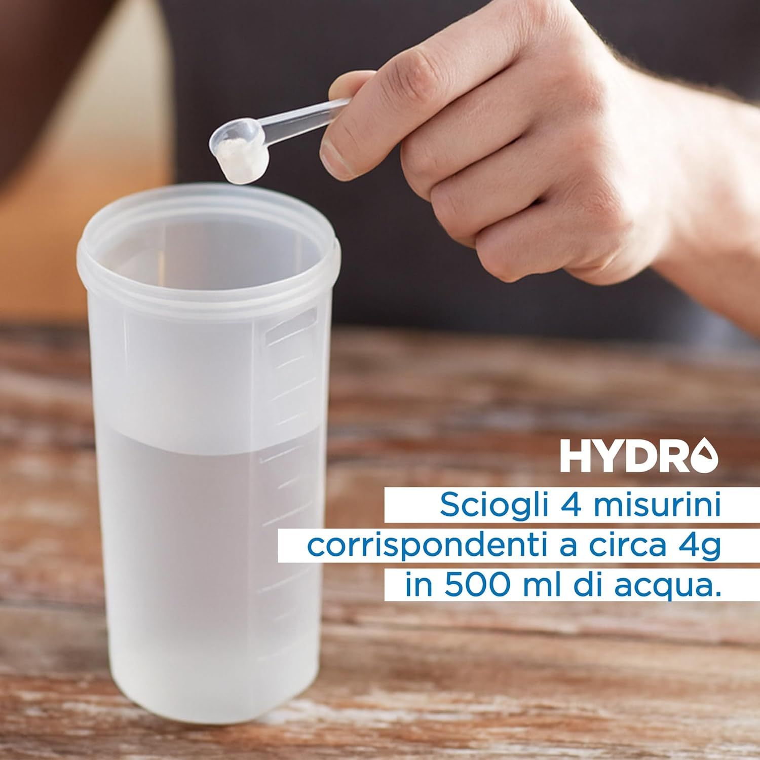 Persona che versa polvere in un bicchiere d'acqua. Testo: HYDRO, sciogliere 4 misurini in 500 ml di acqua.