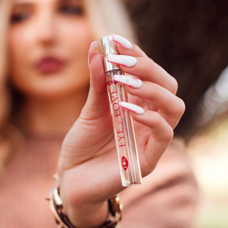 Donna che tiene in mano un flacone di profumo. Scritta: EYE OF LOVE. Flacone con vaporizzatore. Sfondo sfocato.