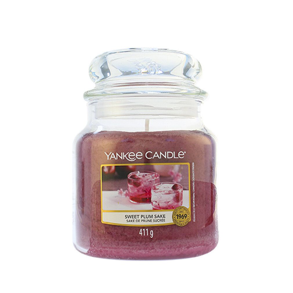 Vasetto di candela con coperchio. Etichetta con immagine e testo: Sweet Plum Sake, 411g. Marchio: Yankee Candle.